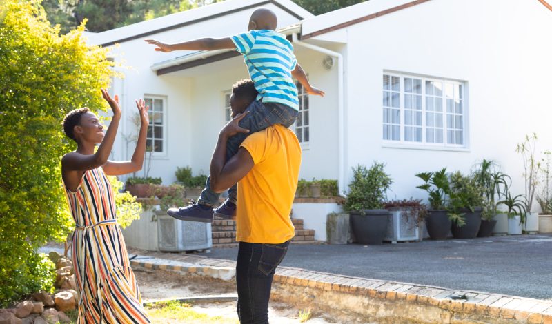 African American woman spending time with her partner who is giving their son a piggyback in the garden. Social distancing and self isolation in quarantine lockdown.