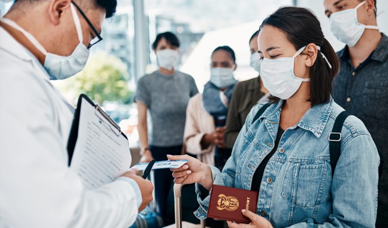 Shot of a woman wearing a mask and giving her passport to a doctor in an airport.