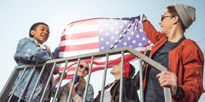 teenagers having fun and waving american flag in skateboard park, hipster style concept